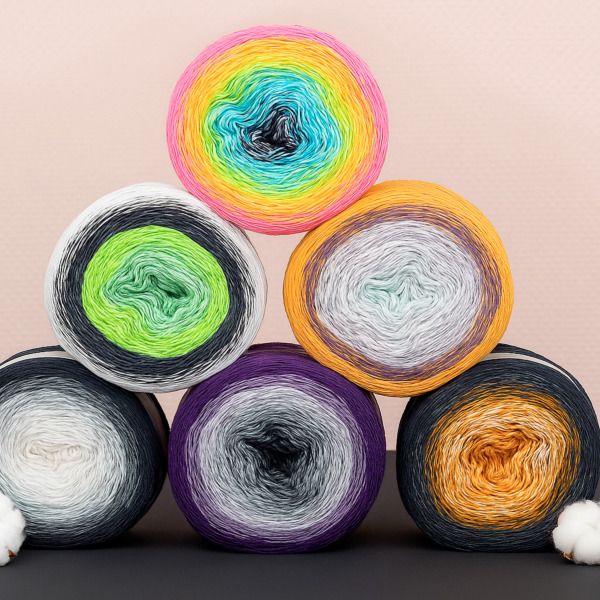 Garencakes van Scheepjes Cotton Whirl in diverse kleurverlopen, gestapeld in een piramide op zwarte ondergrond met katoen details